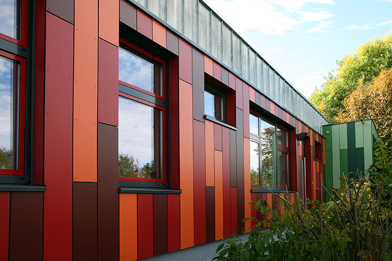 Façade d'un bâtiment avec des plaques de composite en bois rouge, orange, marron de la marque Trespa® Uni Colors